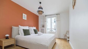 Een slaapkamer met een bed, een nachtkastje, een hanglamp en een raam met gordijnen.