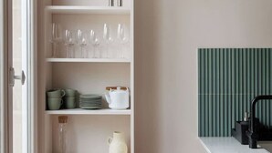 Een keuken met witte kasten, een groene accentmuur en een raam.