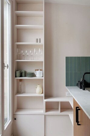 A kitchen with white cabinetry, a green accent wall, and a window. - 8 Joubert -  3BDR Galeries Lafayette (Paris)