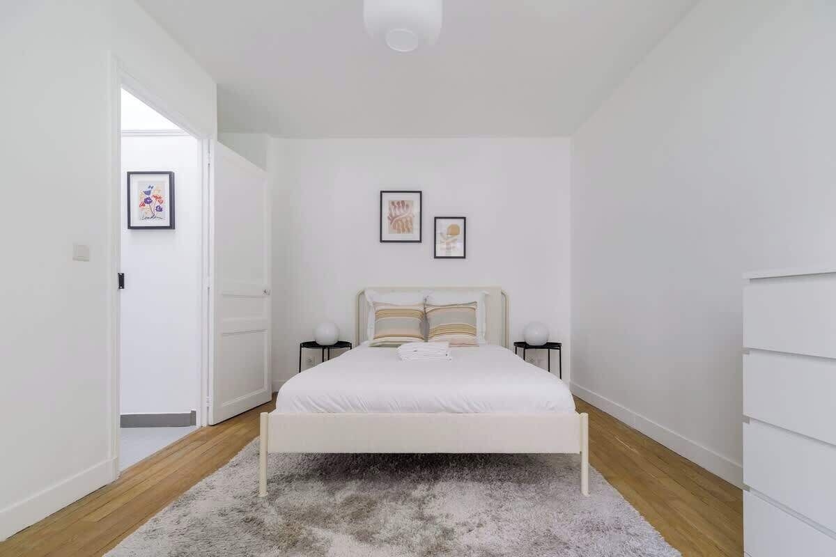 A bedroom with a white bed, two bedside tables, a gray rug, and framed artwork on the wall.