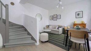 A modern living room with a staircase, a sofa set, a dining table with chairs, and a fireplace. - Charmante maison 6PAX proche Arc de Triomphe (Paris)