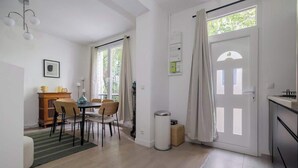 A modern kitchen with a dining area, a trash bin, and a door with a window. - Charmante maison 6PAX proche Arc de Triomphe (Paris)