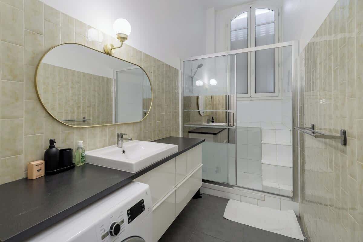 A modern bathroom with a large mirror, a sink, a shower, and a washing machine.