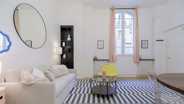 A modern living room with a sofa, a round glass coffee table, a yellow chair, a striped rug, and a large mirror. - Perretti - Spacious Flat 2BDR Paris Neuilly (Neuilly-sur-Seine)