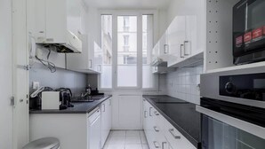A modern kitchen with white cabinetry, a black countertop, and a window providing natural light. - Perretti - Spacious Flat 2BDR Paris Neuilly (Neuilly-sur-Seine)