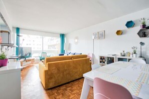 A modern living room with a sofa, a dining table, and a kitchen area. - Dominos - La Defense Family Apartment 10P (Courbevoie)