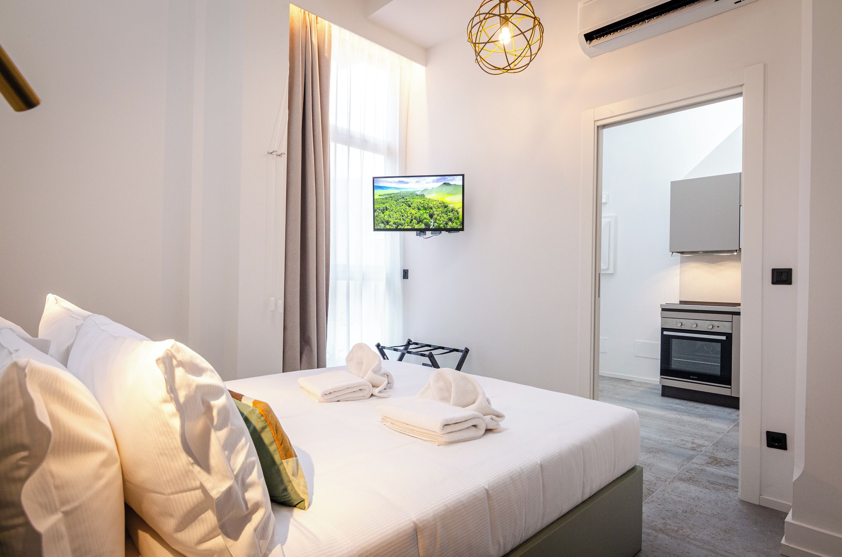Habitació d'hotel amb llit, televisió de pantalla plana, zona de cuina i finestra gran amb cortines.