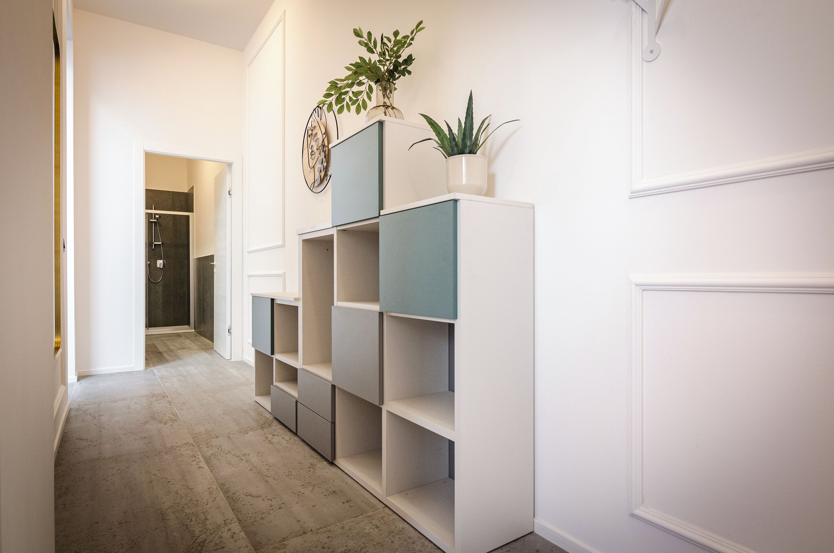 A hallway with a built-in shelving unit, a potted plant, and a door leading to a shower area.