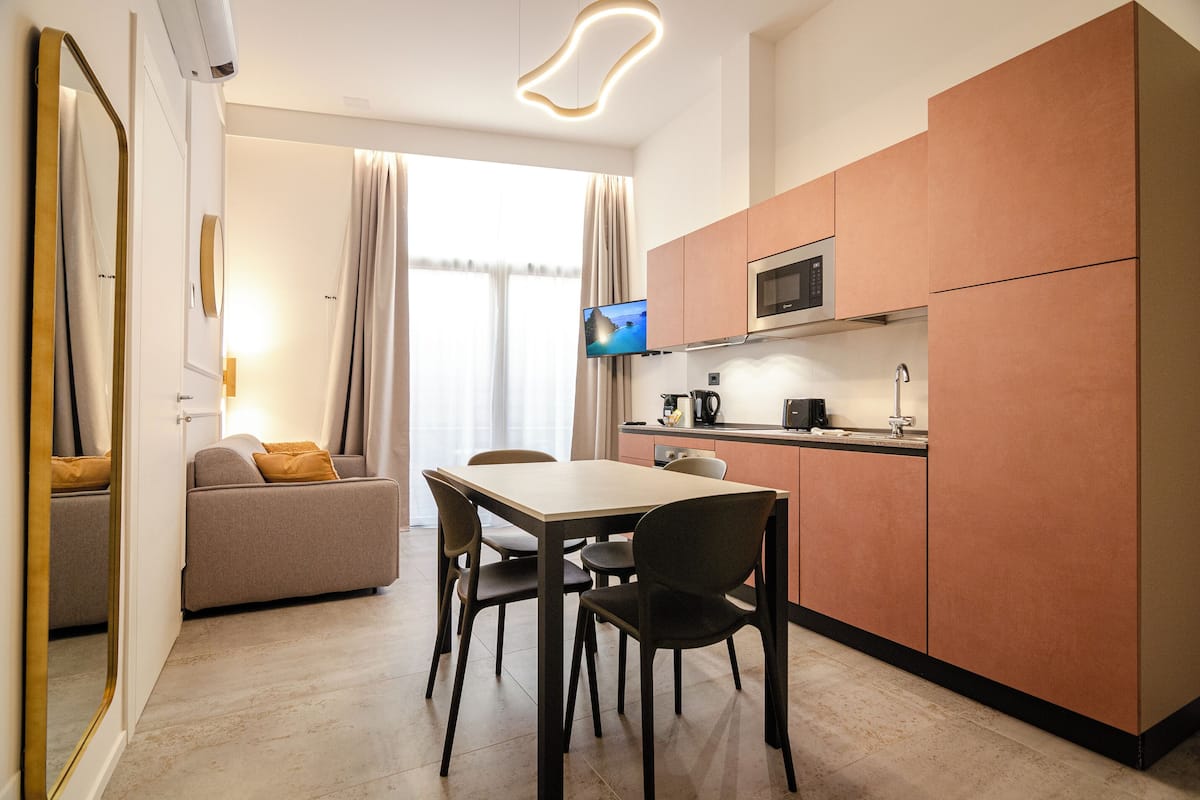 A compact kitchen with a dining area, a flat-screen TV, and a sofa.