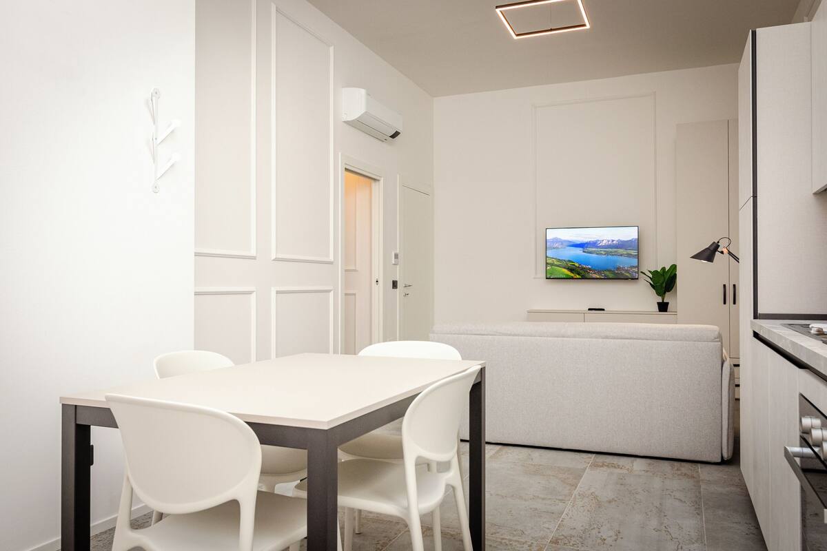 A modern kitchen with a dining area, a flat-screen TV mounted on the wall, and a small potted plant.