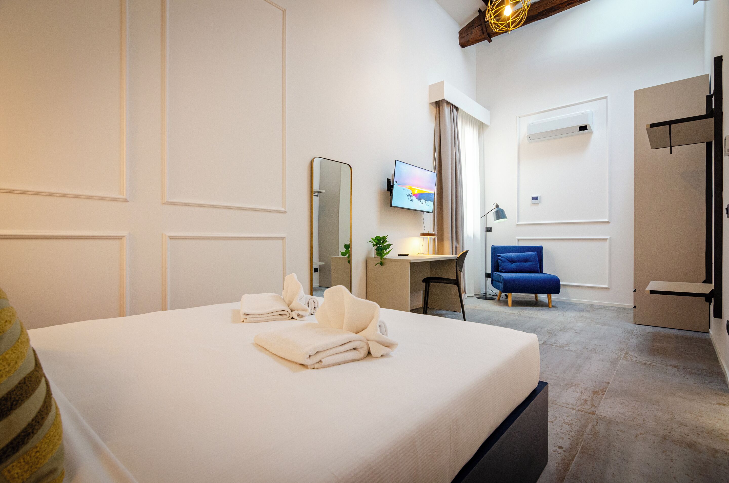 Quarto de hotel com cama, escrivaninha, televisão e cadeira.