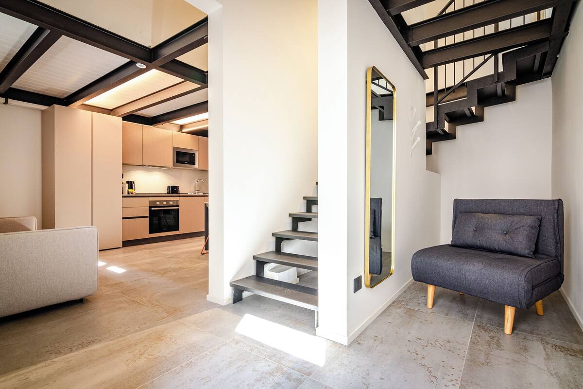 A modern interior with a staircase, a sofa, and a kitchen area.