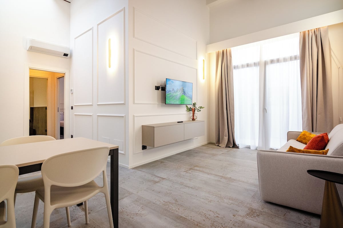 A modern living room with a flat-screen TV, a sofa, a dining table, and chairs.