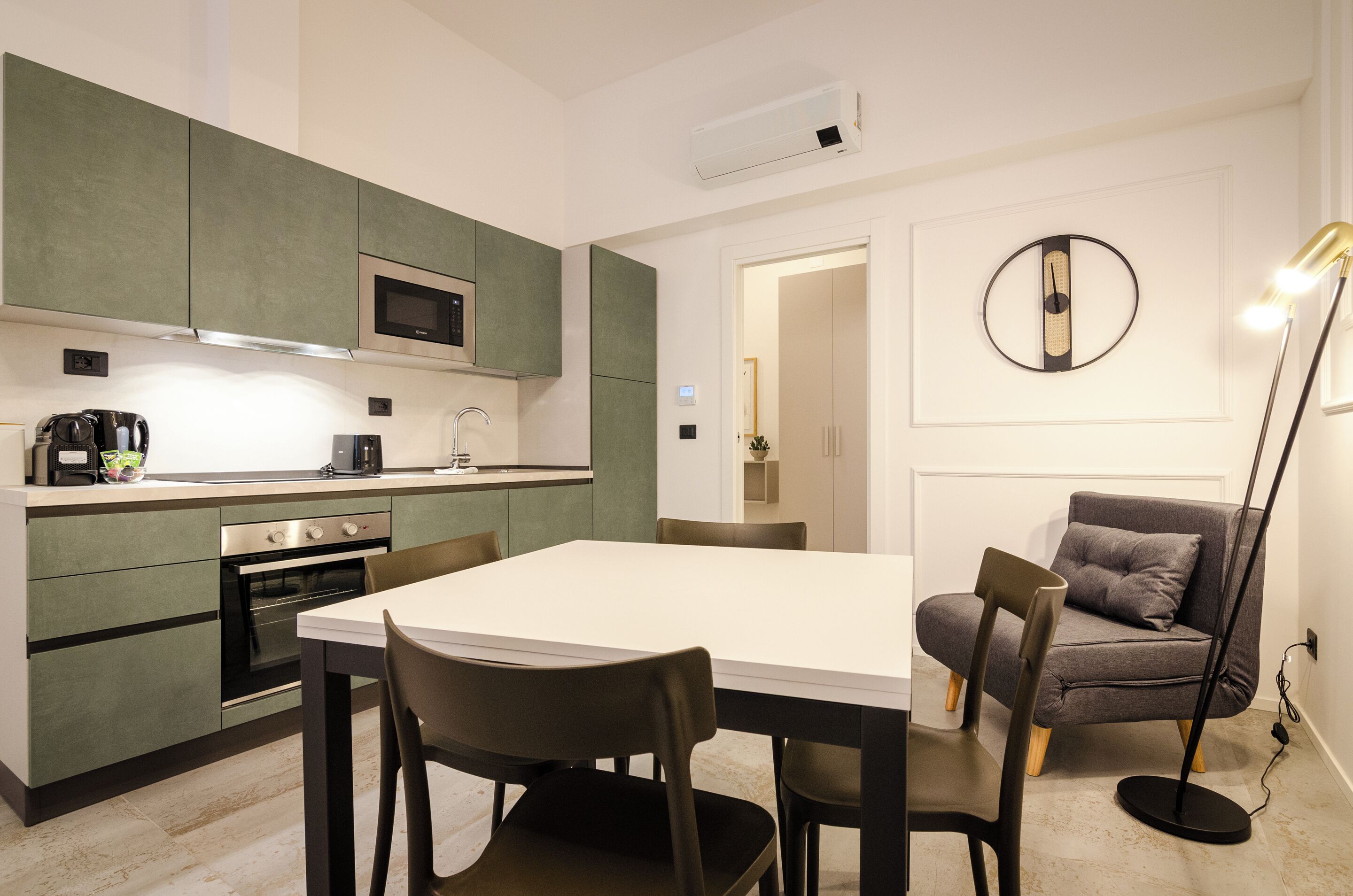 A modern kitchen with a dining area, including a table and chairs, a sofa, and a floor lamp.