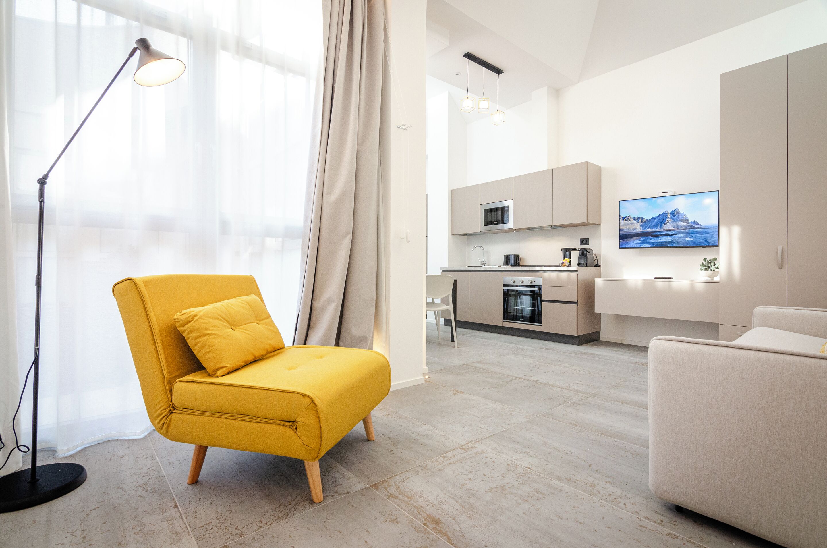 Una sala de estar moderna con un sillón amarillo, una lámpara de pie y un televisor al fondo.