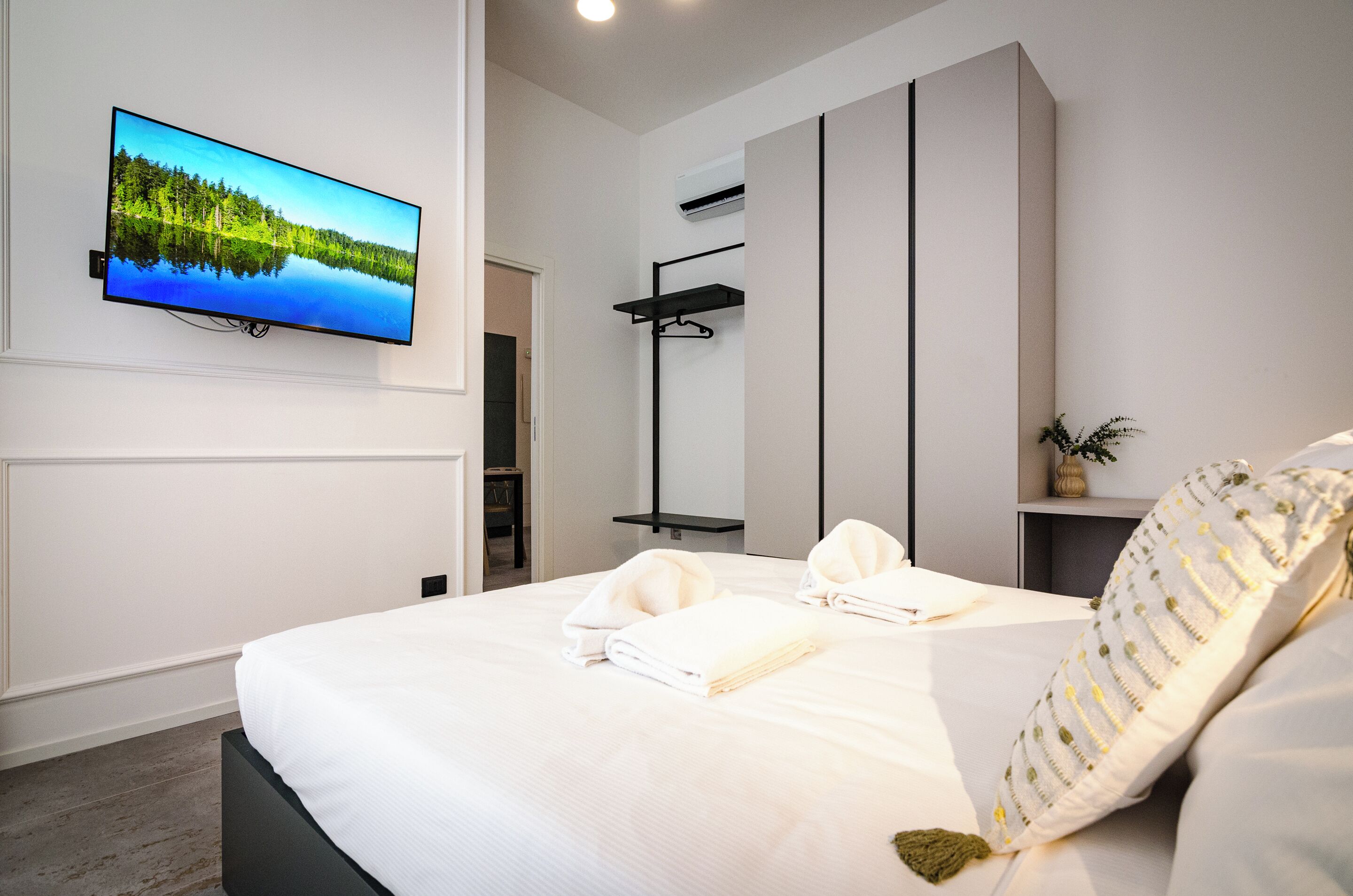 Une chambre d’hôtel moderne avec un grand lit, un téléviseur fixé au mur, une armoire et une petite plante.
