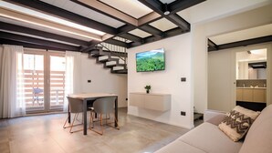 A modern living room with a sofa, a dining table with chairs, a TV mounted on the wall, and a staircase leading to an upper level. - Albani Lofts (Bologna)
