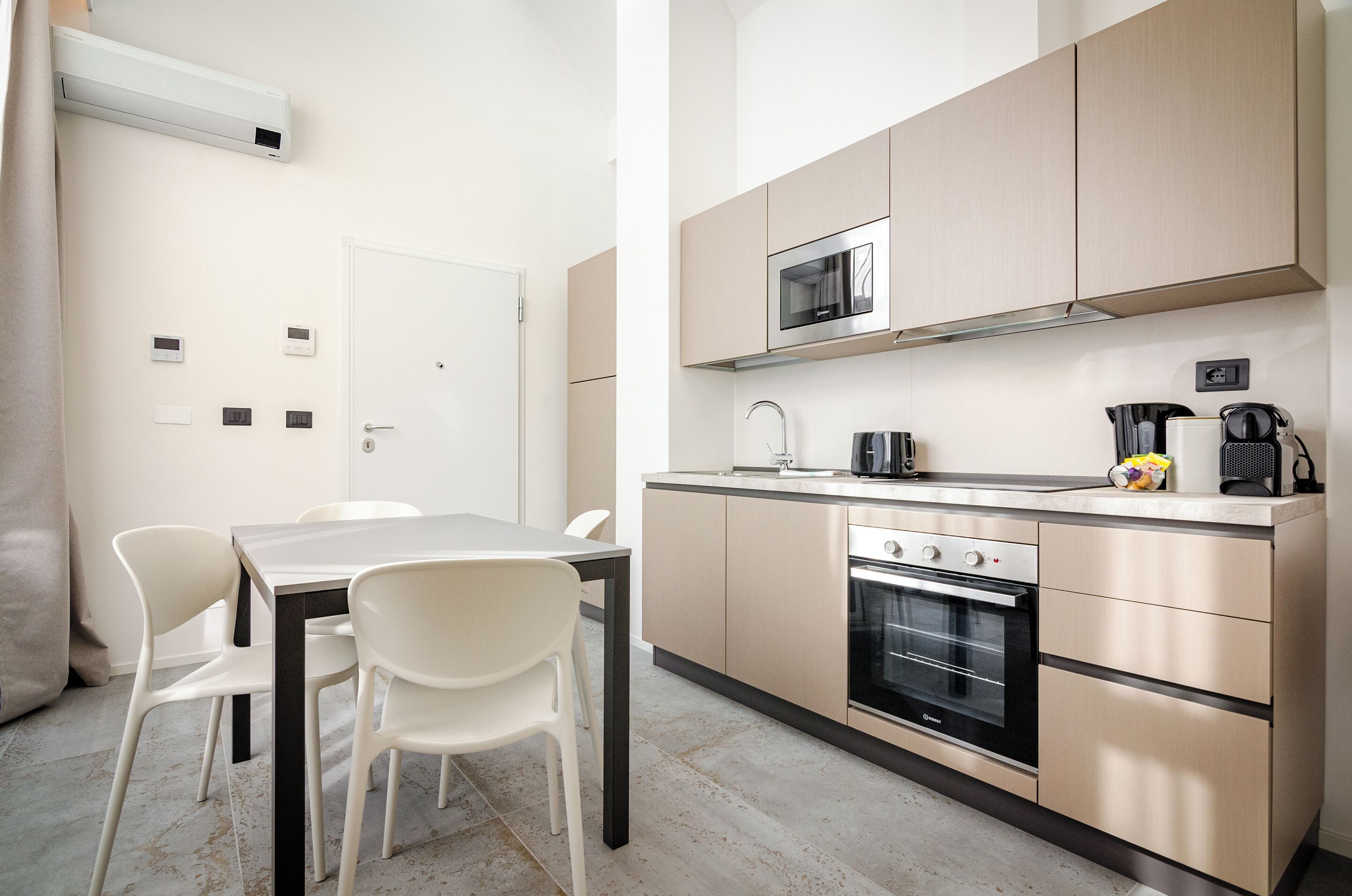 A modern kitchen with a microwave, oven, and coffee maker. There is a dining table with chairs.