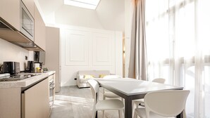 A modern kitchen with a dining area, white furniture, and a large window with curtains. - Albani Lofts (Bologna)