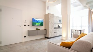 A modern living room with a flat-screen TV, a sofa, a dining table, and a kitchen area with cabinets and a microwave. - Albani Lofts (Bologna)