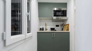 A compact kitchen with a microwave, a stainless steel range hood, and a window with white frames. - Appartement chaleureux proche Notre-Dame - 1BR (Paris)