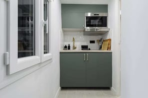 A compact kitchen with a microwave, a stainless steel range hood, and a window with white frames. - Huchette - Appartement chaleureux proche Notre-Dame (Paris)
