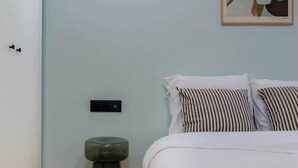 A bedroom with a bed, a bedside table, a wall-mounted light, and a painting. - Appartement chaleureux proche Notre-Dame - 1BR (Paris)