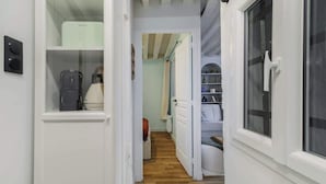 A narrow hallway with a white door, a window, and a shelf with kitchen appliances. - Appartement chaleureux proche Notre-Dame - 1BR (Paris)