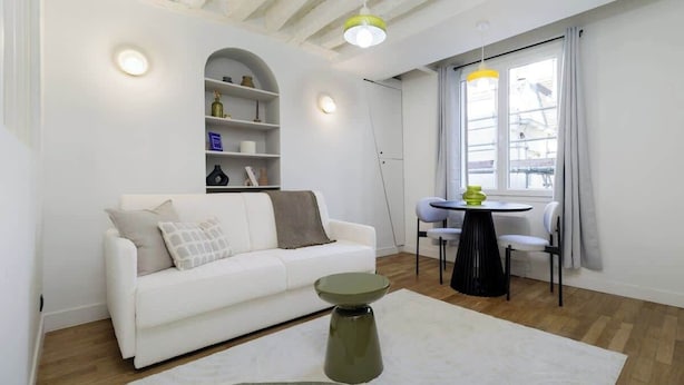 A modern living room with a white sofa, a round coffee table, and a dining area with a table and chairs. - Appartement chaleureux proche Notre-Dame - 1BR (Paris)