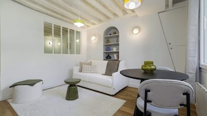 A modern living room with a white sofa, a round table, a green ottoman, and a white rug. - Appartement chaleureux proche Notre-Dame - 1BR (Paris)