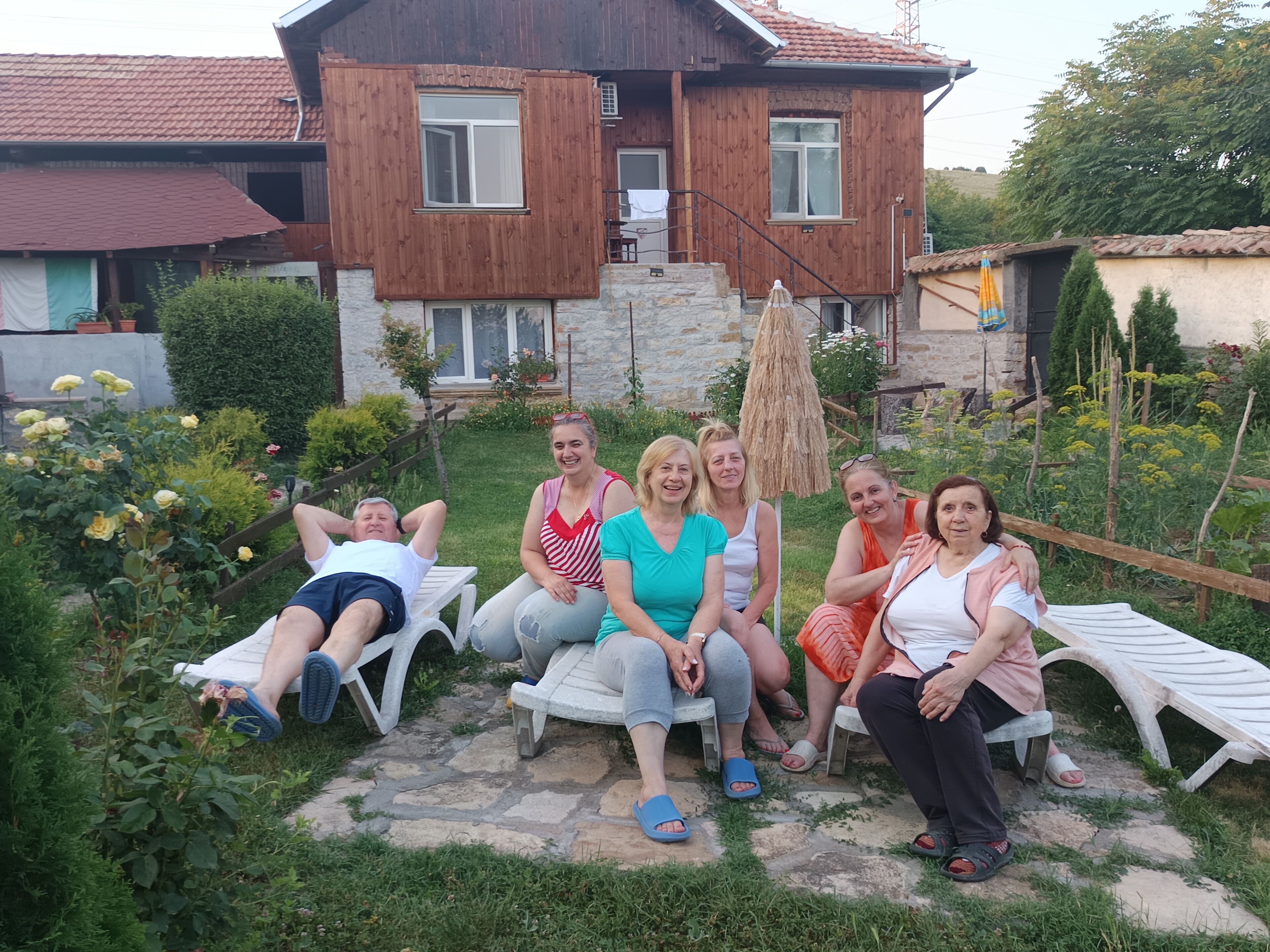 Un grupo de personas sentadas en sillones de jardín con una casa de madera al fondo.
