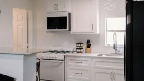 A modern kitchen with white cabinets, a black microwave, a gas stove, and a black refrigerator. - Urban Chic 1 BR - Downtown Abilene -  Data Center (Abilene)