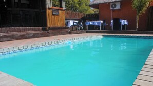 Una piscina amb vora de rajola, envoltada per un terra de maó. Hi ha taules i caires a l'exterior, i un edifici amb teulada de palla al fons.