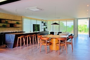 A modern kitchen with a bar, dining area with round table and chairs, and a large window with a view of greenery. - Luxury Mansion VILLA MARIA (brand new) (Tibau do Sul- RN)