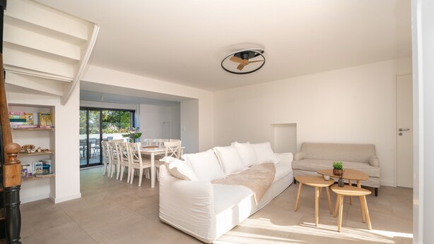 A modern living room with a white sofa, a dining table with chairs, and a ceiling fan. - Holiday Home 'Refuge du Sentier Sauvage' with Private Terrace (Belz)