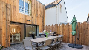 A wooden deck with a table and chairs, a grill, and a green umbrella. - Holiday Home 'Refuge du Sentier Sauvage' with Private Terrace (Belz)