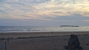 A beach with a rocky outcrop in the foreground, a sandy shore, and calm sea. - Holiday Home 'Refuge du Sentier Sauvage' with Private Terrace (Belz)