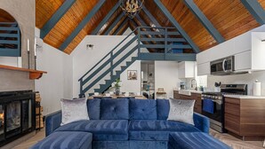 Un soggiorno moderno con un divano a divano blu, un camino, una cucina con forno a microonde e fornello, e un soffitto in legno.