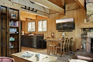Ein rustikales Holzhaus-Interieur mit einem Essbereich aus Holz, einer Küche und einem Kamin aus Stein.