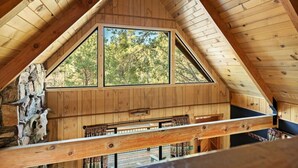 A wooden interior with a sloped ceiling, a large window, and a stone wall. - The Silver Coyote, w/ Bear Mtn Views & Firepit (Big Bear Lake)
