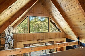 Ein Holzinnenraum mit schrägverdeckter Decke, einem großen Fenster und einer Steinwand.