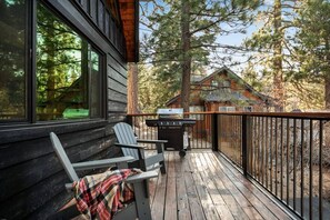 Eine Holzterrasse mit zwei Adirondack-Stühlen und einem Grill.