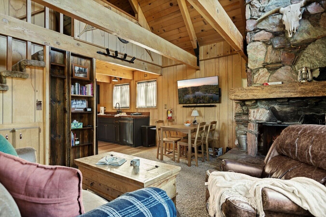 Een rustiek chaletinterieur met een woonkamer, keuken en een stenen open haard.