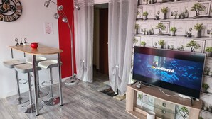A modern living room with a TV, a red accent wall, a floor lamp, a dining area, and a wall with potted plants. - Large T5 for 7 people (Angers)