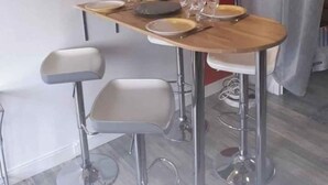 A dining area with a wooden table, four barstools, a wall clock, and a modern pendant light. - Large T5 for 7 people (Angers)