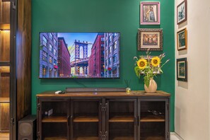 A television mounted on a green wall, a wooden cabinet below, and a vase with sunflowers. - New Modern Luxury 6Br Villa In Canggu - Rooftop - Ricefields - Large Groups (Tabanan)