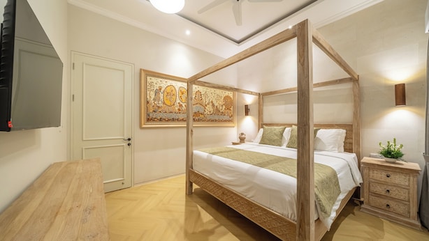 A four-poster bed with a wooden frame, a bedside table with a lamp, a wall-mounted TV, and a decorative painting. - Modern Luxury 6Br Villa In Canggu - Rooftop - Ricefields - Large Groups (Tabanan)