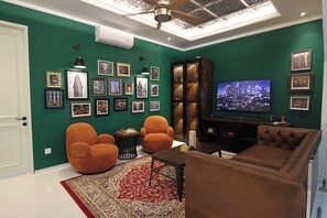 A living room with green walls, multiple framed pictures, a television, and two orange armchairs. - New Modern Luxury 6Br Villa In Canggu - Rooftop - Ricefields - Large Groups (Tabanan)