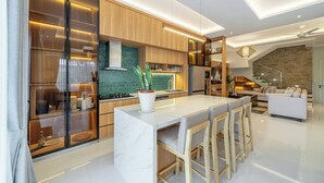 A modern kitchen with a central island, bar stools, and a dining area with a sofa. - Modern Luxury 6Br Villa In Canggu - Rooftop - Ricefields - Large Groups (Tabanan)