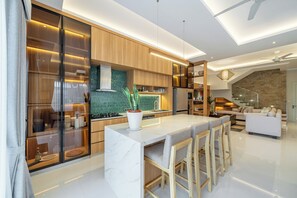 A modern kitchen with a central island, bar stools, and a dining area with a sofa. - Modern Luxury 6Br Villa In Canggu - Rooftop - Ricefields - Large Groups (Tabanan)